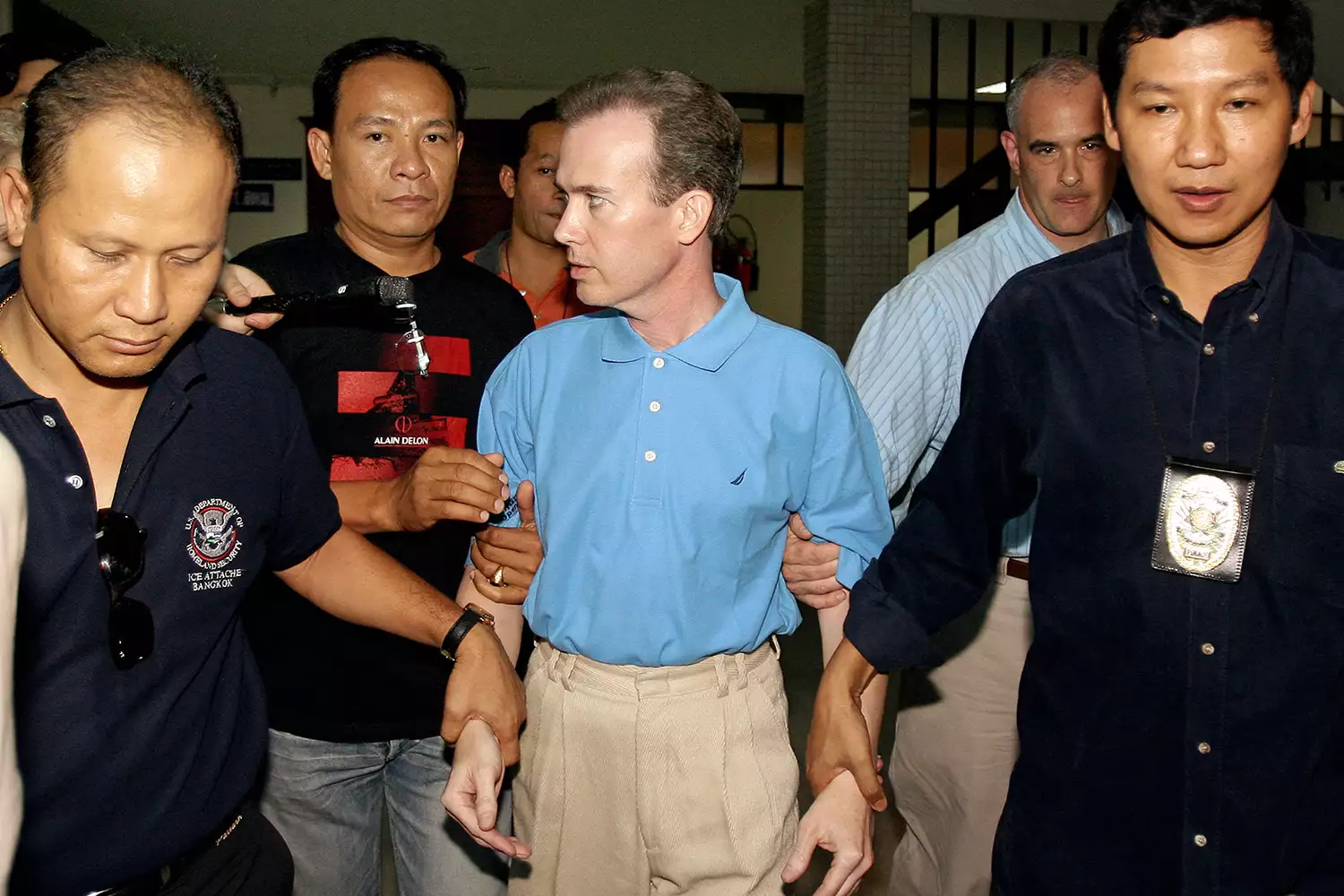 Who is behind the death of the six-year-old beauty queen? 3 Thai police officials escort away US teacher John Mark Karr (C) at the Thai Immigration Department in Bangkok, 17 August 2006. Police said 17 August that Karr, arrested in Thailand 16 August, confessed to killing six-year-old "beauty queen" JonBenet Ramsey a decade ago in the United States but said her death was unintentional. AFP PHOTO/ Saeed KHAN